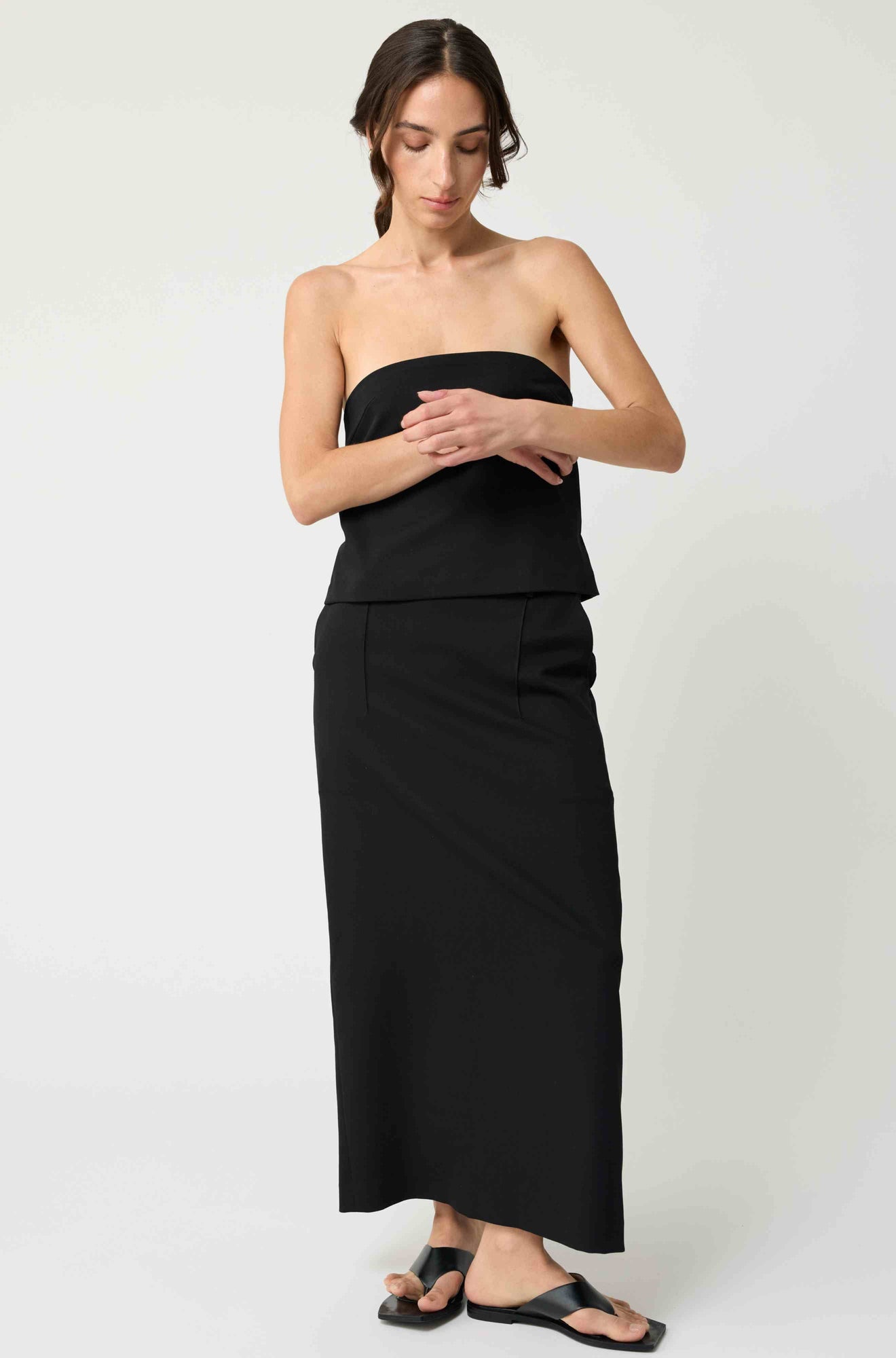 Woman wearing a black strapless top with a matching black skirt on a light grey background