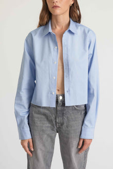 Person wearing a light blue button-up shirt and gray jeans on a white background
