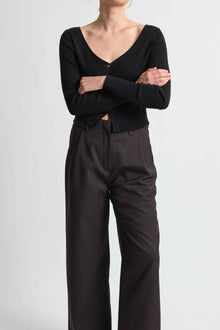 Person wearing a black long-sleeve top and dark brown pants on a light gray background