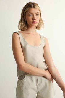 Woman wearing a beige sleeveless top and pants against a plain background