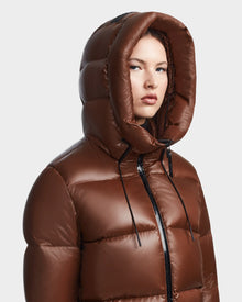A person wearing the Rudsak RITA S - L123527 Cohiba, a shiny brown womens hooded down puffer with a large hood, looks slightly to the side against a plain light background.
