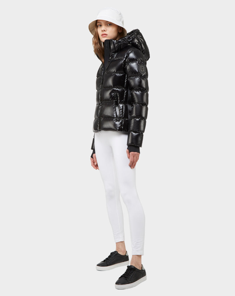 A woman wearing the MARE - 8121011 BLACK ultra-light women's down puffer jacket, white bucket hat, white leggings, and black sneakers stands against a light gray background.