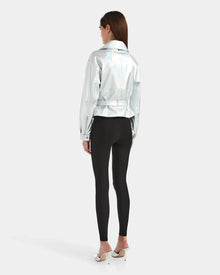 A woman faces away, wearing the Rudsak ARIELLE - 8124052 Iridescent Cotton White jacket, black leggings, and white high heels against a plain white background.