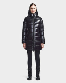 A woman faces forward against a white background, wearing the RUDSAK MARNIE LONG - 8122519 BLACK jacket with a hood, paired with black leggings and black winter boots.