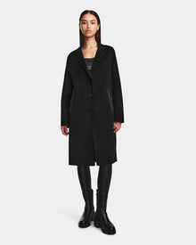A woman faces forward, wearing the Rudsak ARLA - 8124579 Black wool coat with leather sleeves, paired with black leggings and boots, her hands by her sides against a plain white background.