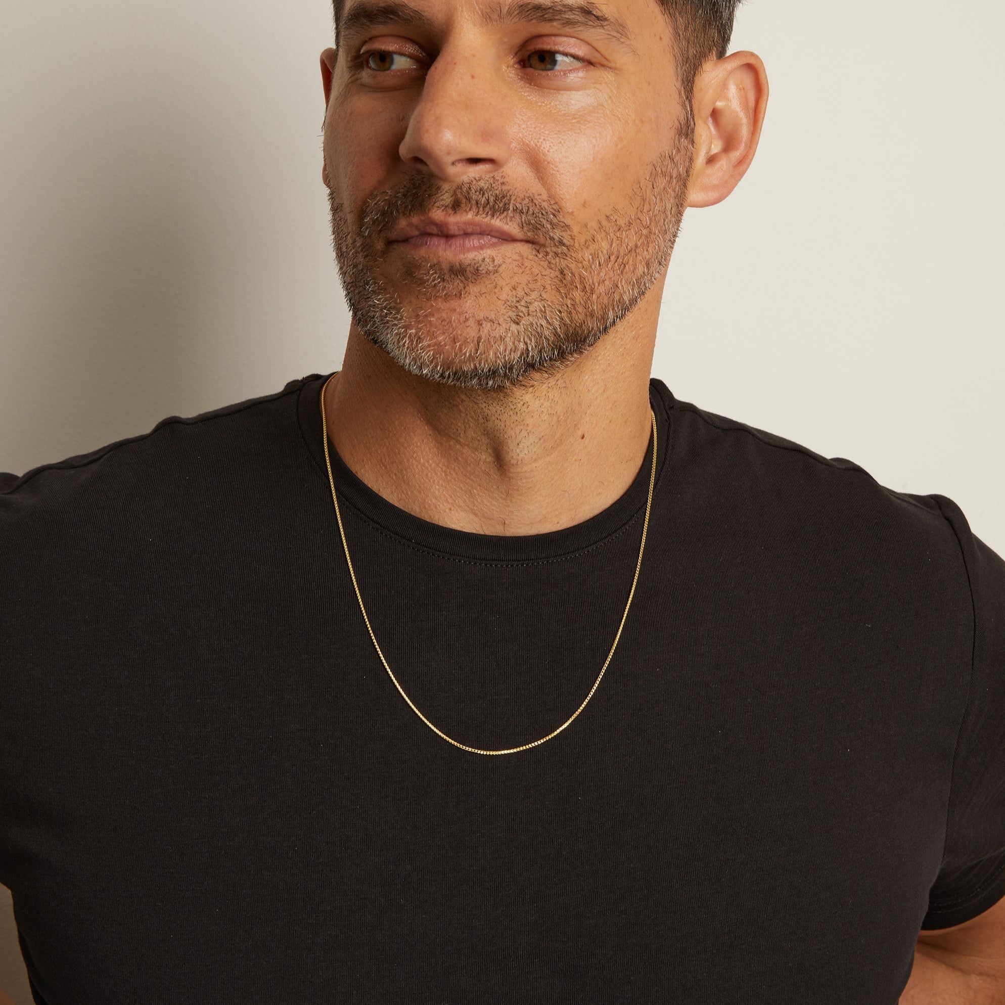 Model. Man wearing a black t-shirt and gold necklace against a plain background