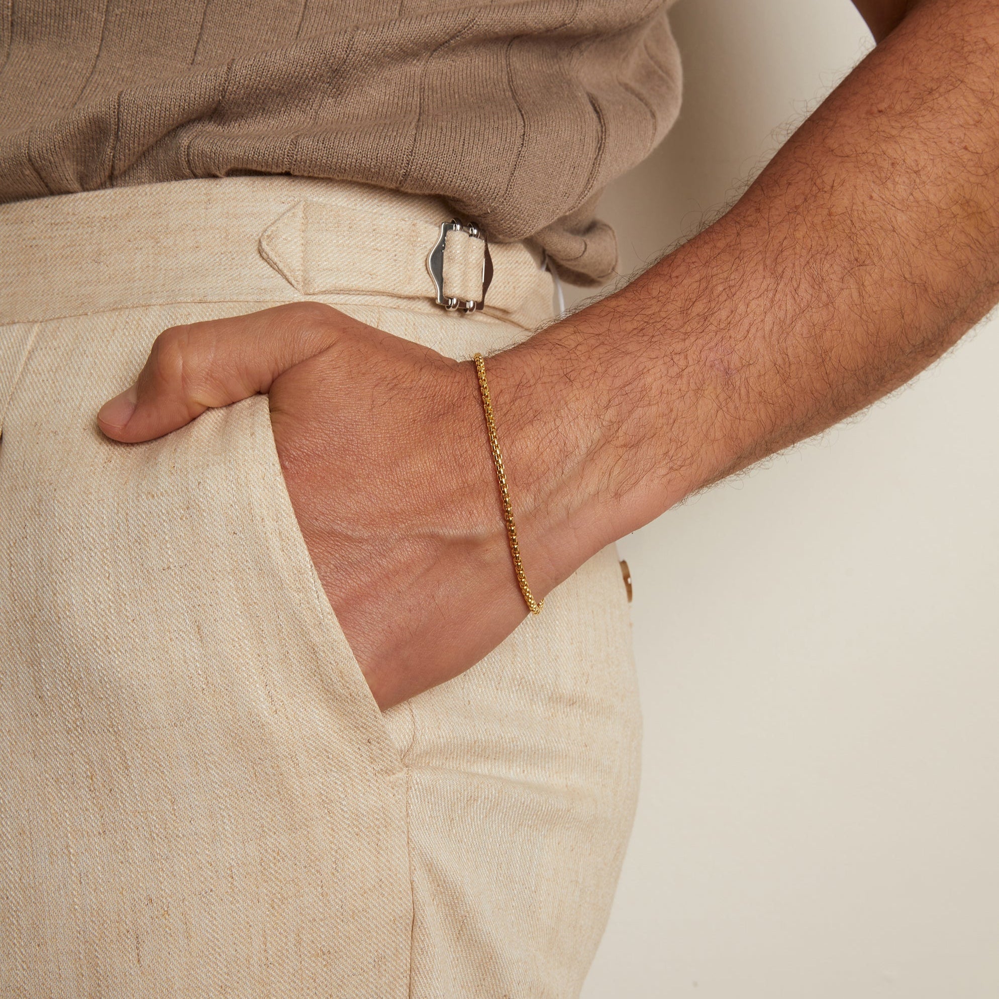 Person wearing a gold bracelet with beige pants and shirt.