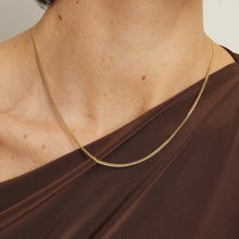 Model. Gold chain necklace worn by a person with a brown top