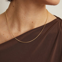 Model. Gold necklace on a person wearing a brown top against a neutral background
