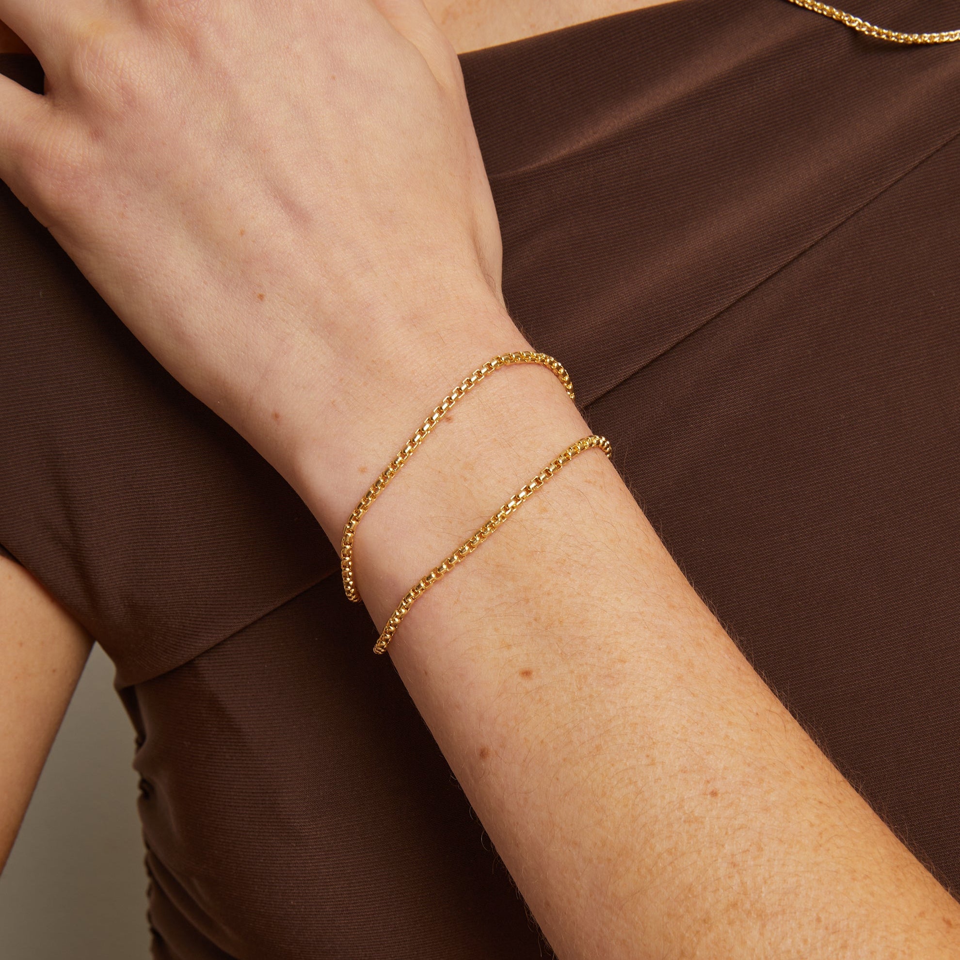 Model. Gold bracelet on a wrist against a brown background