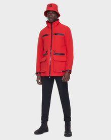 Wearing the RUDSAK JACY - 6122000 POPPY RED raincoat and a matching red bucket hat, paired with black pants and boots, a person stands against a plain white background.