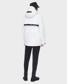 A person in the RUDSAK JACY - 6122000 WHITE water-resistant trench coat, paired with black pants, boots, and a bucket hat, faces away from the camera against a plain background.