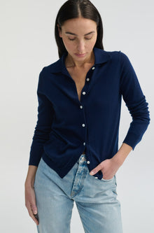 Woman wearing a navy blue cardigan over a white shirt with light blue jeans on a plain background